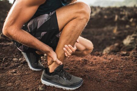 Achilles injury on running outdoors. Man holding Achilles tendon by hands close-up and suffering...