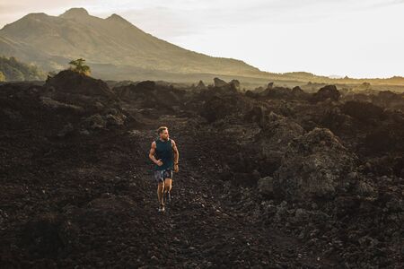 Young athlete man trail running in mountains in the morning. Amazing volcanic landscape of Bali...