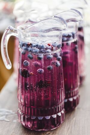 Jug with fresh cold blueberry lemonade with bubbles close-up. Summer freshness beverage