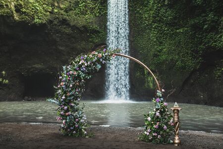 Round metal wedding arch decorated with purple and green flowers on Tibumana waterfall, Bali. Modern style, wedding and love concept.の写真素材