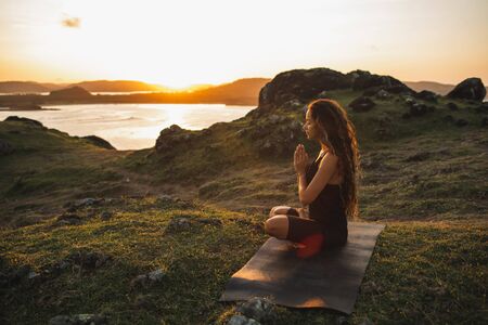 Woman doing yoga alone at sunrise with mountain and ocean view. Harmony with nature. Self-analysis and soul-searchingの写真素材