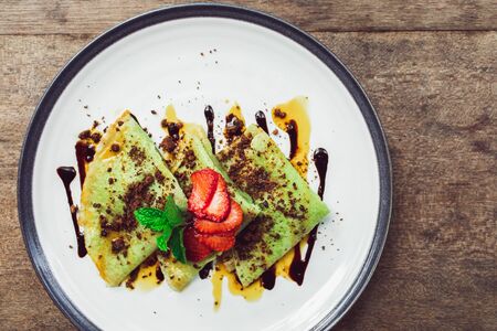 Traditional indonesian green pancakes topping with chocolate and strawberries slices. Breakfast food concept. Top view.の写真素材