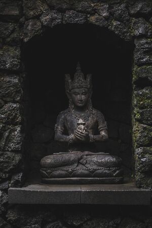 Balinese deity statuette on dark stone background. Hindu culture in Bali. Handmade stone carving.