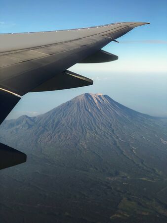 Aerial view of Agung volcano peak in Bali from plane window. Clear weather and aircraft wing.