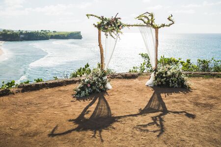 Sunset wedding ceremony arch with wooden branches and flower decoration and white cloth canopy. View of Balangan cliff in Bali. Wedding with ocean view.の写真素材