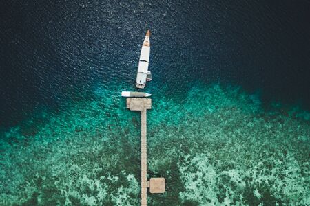 Aerial view of pier with yacht on tropical island with coral reef coastline. Cruise and luxury boat travel concept. Directly from above.の写真素材