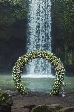 Wedding ceremony on Tibumana waterfall, Bali. Round arch with fresh flowers in jungle. Unusual nature wedding concept.の写真素材