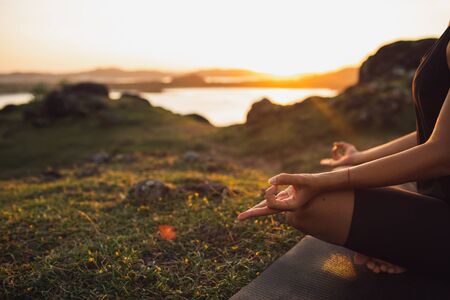Healthy Lifestyle and Yoga Concept. Close-up hands. Woman do yoga outdoors at sunrise in lotus position. Woman exercising and meditating in morning. Nature background.の写真素材