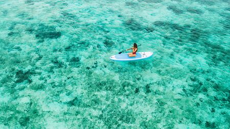Woman sitting on sup board and enjoying turquoise transparent water and coral reef. Tropical travel,...