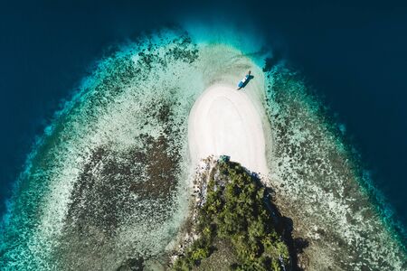 Aerial view of white sand beach on small tropical coral reef island with tourist diving boat....