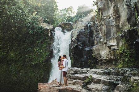 Young couple in love kissing with amazing view of Tegenungan cascade waterfall. Happy together, honeymoon in Bali. Travel lifestyle.の写真素材