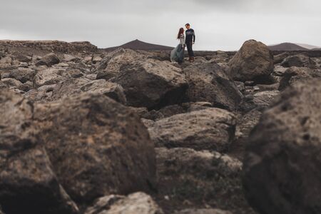 Couple in love walking in Iceland. Stone volcanic desert around, in the middle of nowhere. Dramatic nordic landscape, cold weather. Wearing in traditional wool sweaters, jeans and gray skirt.の写真素材