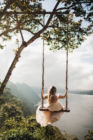 Woman swinging outdoors over amazing mountain, jungle and lake view over a cliff in Bali Wanagiri hidden hill. Freedom and wanderlust concept. Popular balinese tourist landmark and photo point.の写真素材