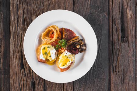 Eggs benedict with onion rings, sausage, baked potato and roasted mushrooms on wooden background top viewの写真素材