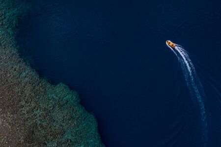 Aerial view of tourist boat on surface of deep blue tropical ocean coastline with coral reef.の写真素材