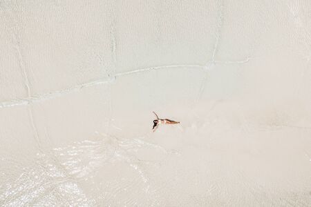 Aerial drone shot of woman lying in water on white sand beach and enjoying vacations. Tropical...