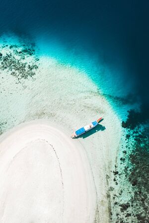 Aerial view of white sand beach on small tropical coral reef island with tourist diving boat....