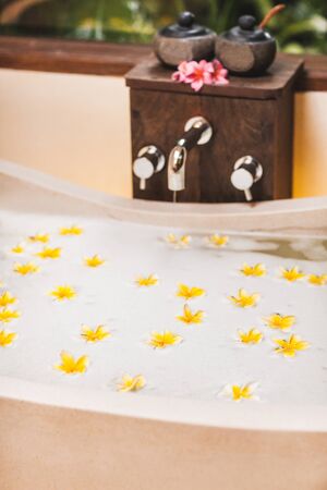 Bathtub with foam bubbles and yellow flowers close-up. Flower bath tub in spa, wellness treatment...