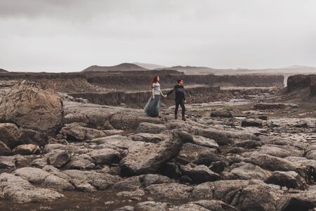 Couple in love walking in Iceland. Stone volcanic desert around, in the middle of nowhere. Dramatic nordic landscape, cold weather. Wearing in traditional wool sweaters, jeans and gray skirt.の写真素材
