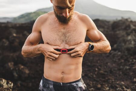 Male runner wearing professional chest heart rate monitor and preparing for trail running outdoors. Topless body close-up and smart watch or fitness tracker on hand.の写真素材