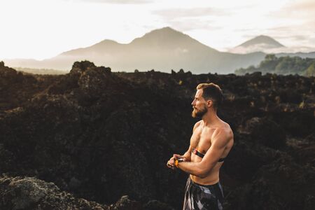 Athletic man start running program on smart watch or fitness tracker. Training topless and using chest heart rate monitor. Trail running outdoors.の写真素材