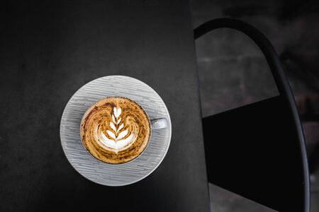 Gray cup of fresh cappuccino with chocolate on foam on dark black metal table background. Empty...