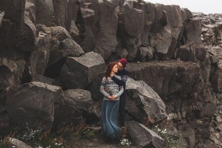 Couple in love in Iceland. Stone volcanic background. Dramatic nordic landscape, cold weather. Wearing in traditional wool sweaters, jeans and gray skirt.の写真素材