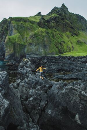 Woman walking by black stone rocky volcanic coastline of Vestmannaeyjar island in Iceland. Northern...