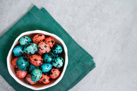 Painted red and blue quail eggs for Easter in small ceramic plate on green napkin on gray concrete...