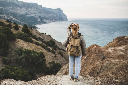 Backpacker hippie woman happy to enjoy amazing sea and mountain view from hill. View from behind....