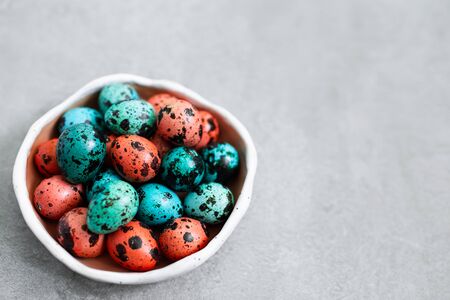 Painted red and blue quail eggs for Easter in small ceramic plate on gray concrete background. Empty...
