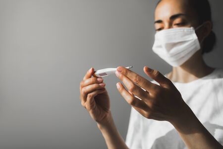 Patient in medical mask checking temperature on thermometer. Covid-19 and Flu Virus Prevention....