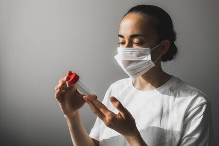 Doctor in medical mask holding in hands test tube with coronavirus smear. Analysis in laboratory. COVID-19 pandemic crisis in the world.の写真素材