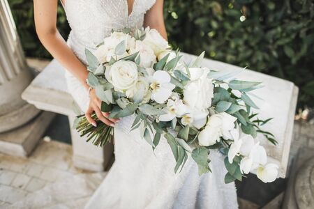 Bride holding in hands elegant blooming bouquet on wedding ceremony. White roses, orchids and greens close up.の写真素材