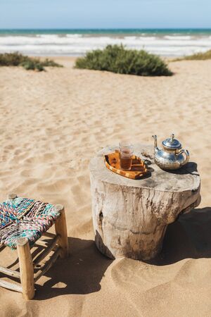 Traditional moroccan mint tea and old silver teapot on wooden table outdoors. Beach and ocean view.の写真素材