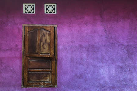 Bright purple shabby wall with closed wooden shutters window. Colorful architecture, old and vintage style. Empty place for text.の写真素材