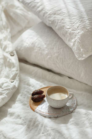 Cup of fresh coffee in bed on ceramic tray, morning mood. Linen cotton textile bedclothes. Organic...