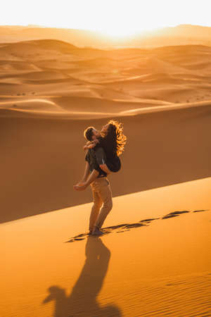 Young happy couple in Sahara desert dunes, Morocco. Happiness, freedom and escape concept. Amazing warm sunset, natural emotions.の写真素材