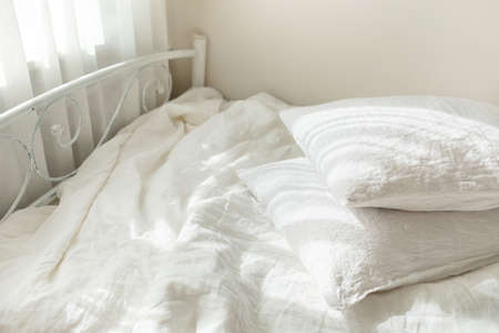 White linen textile bedclothes. Pile of pillows. Cozy bedroom interior and beautiful morning light. Pastel color. Trendy organic natural linen.の写真素材