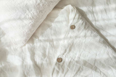 Trendy organic natural linen bedclothes with wooden buttons closeup. Bedding, morning light, bedroom...