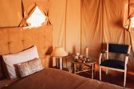 Interior of modern luxury glamping tent bedroom in camp in Morocco. Orange tone. Eco design concept, natural and wooden elements in style. Tray with traditional moroccan tea.の写真素材