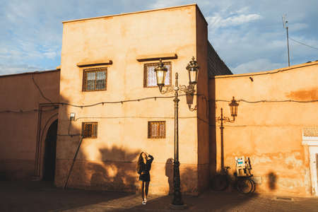 Young beautiful woman walking on Marrakesh street. Red city, terracotta color background. Sunset light. Fashion lifestyle.の写真素材