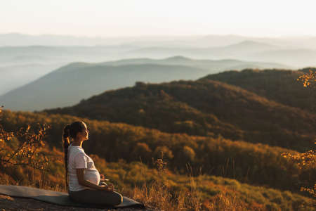 Pregnant woman in lotus position do yoga alone outdoors. Amazing autumn mountain view at sunset....