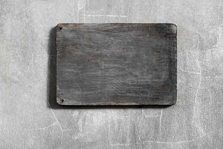 Dark gray wooden empty board hanging on shabby concrete cement wall. Place for logo, sign or text.