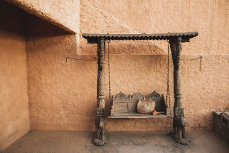 Beautiful wooden carved swing on chains. Handmade wicker straw bag and leather case for vintage photo camera. Terracotta wall.の写真素材