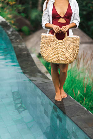 Woman near swimming pool holding in hands handmade straw wicker beach bag. Eco-friendly and zero...