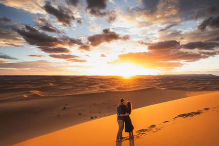 Couple in love kissing in Sahara desert dunes, Morocco. Happiness, freedom and escape concept. Amazing warm sunset with beautiful colorful clouds.の写真素材