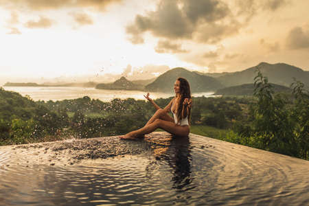 Dream journey in Asia. Woman sitting on edge luxury infinity pool an enjoying amazing mountain, rice...