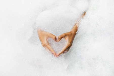 Woman hands in heart shape in bath full of foam bubbles close-up. Spa beauty treatment. Love symbolの写真素材