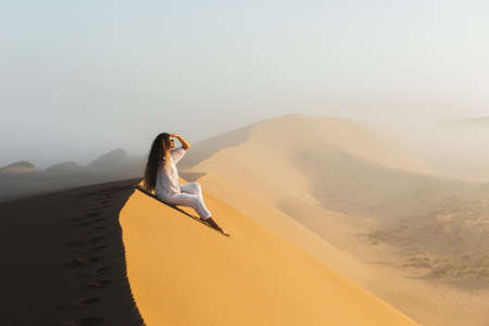 Dream destination, travel and wanderlust concept. Happy woman inspired by fantastic sunrise in Sahara desert sand dunes, Morocco. Mist in morning and warm light.の写真素材